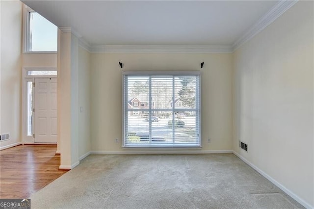 empty room with baseboards, visible vents, carpet floors, and crown molding
