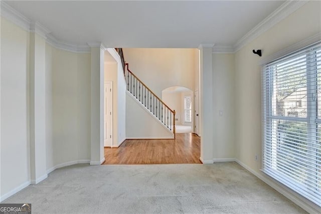 carpeted empty room featuring a healthy amount of sunlight, crown molding, stairs, and arched walkways