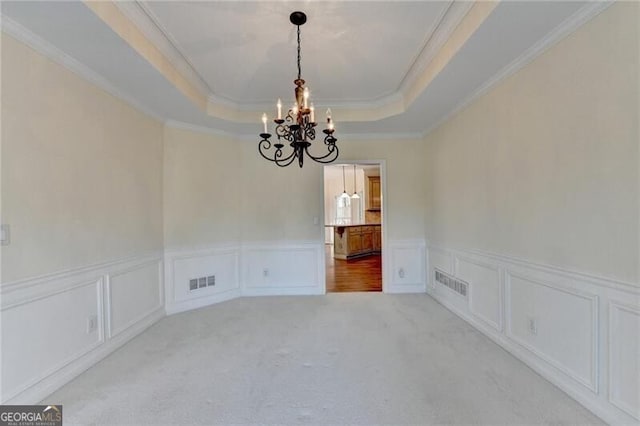 unfurnished dining area featuring a chandelier, a tray ceiling, crown molding, visible vents, and a decorative wall