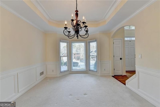 unfurnished dining area featuring a tray ceiling, a decorative wall, ornamental molding, arched walkways, and wainscoting