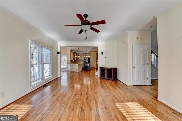 unfurnished living room featuring ornamental molding, baseboards, light wood finished floors, and ceiling fan with notable chandelier
