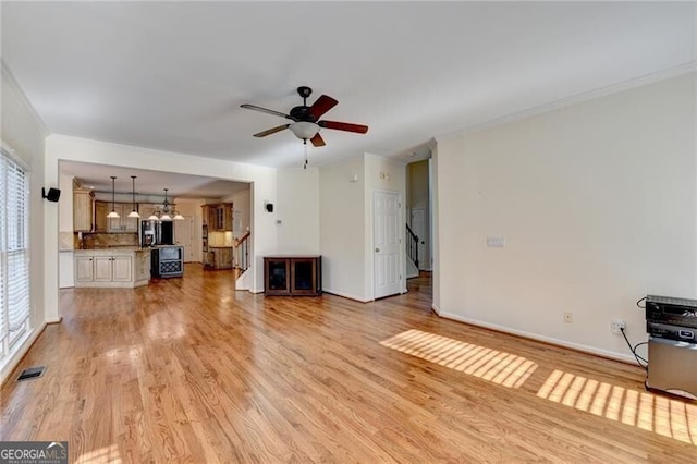 unfurnished living room with ornamental molding, light wood-type flooring, baseboards, visible vents, and a ceiling fan