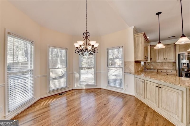 kitchen featuring light stone counters, tasteful backsplash, an inviting chandelier, light wood finished floors, and stainless steel fridge