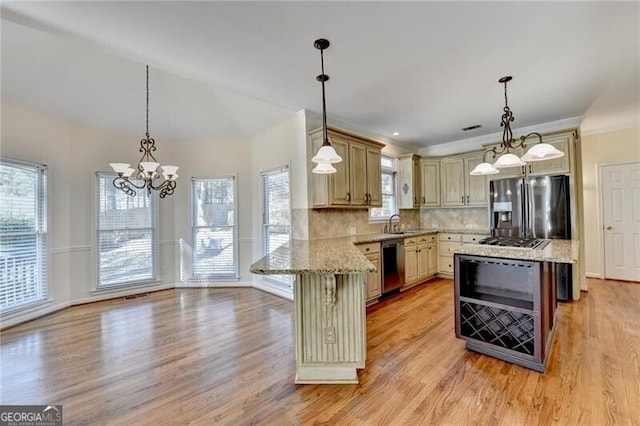 kitchen featuring a sink, a chandelier, stainless steel appliances, light wood-type flooring, and a peninsula