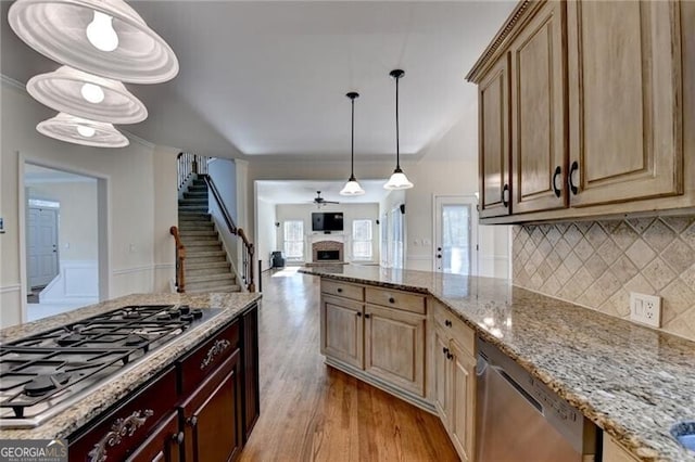 kitchen with light stone countertops, stainless steel appliances, a fireplace, tasteful backsplash, and light wood-style flooring