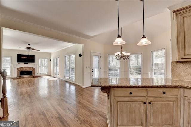 kitchen with light brown cabinetry, ceiling fan with notable chandelier, a fireplace, and light wood finished floors