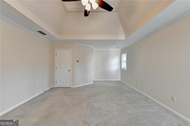 carpeted empty room featuring a raised ceiling, crown molding, a ceiling fan, visible vents, and baseboards