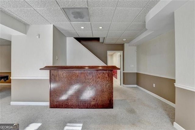 bar featuring a paneled ceiling, carpet flooring, a bar, and baseboards