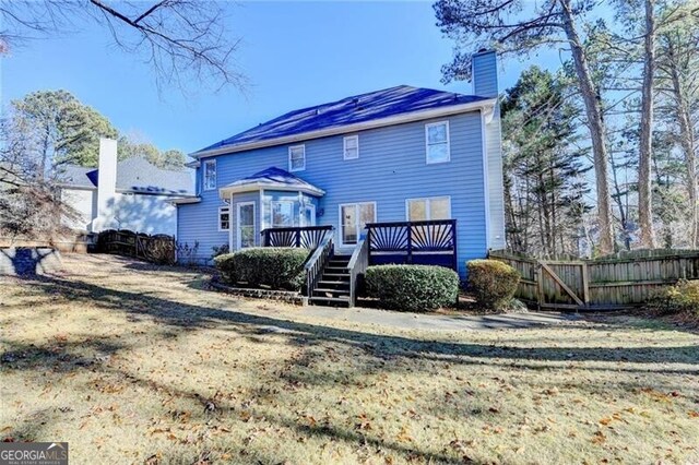 back of house with a chimney, fence, a wooden deck, and a yard