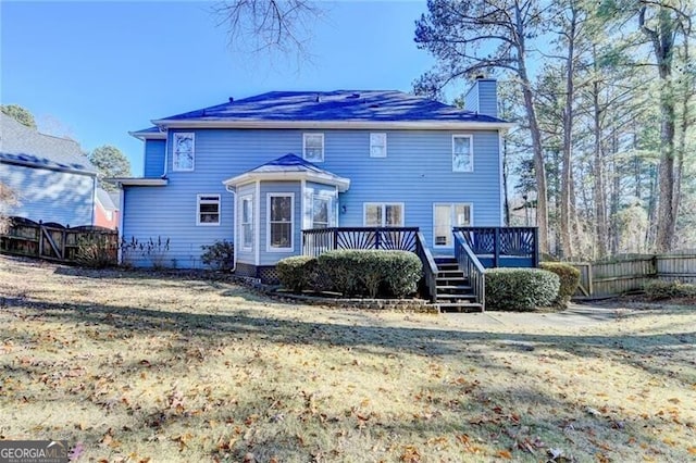 rear view of house with a lawn, a wooden deck, a fenced backyard, and a chimney