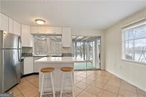 kitchen with freestanding refrigerator, white cabinetry, light tile patterned floors, and a breakfast bar