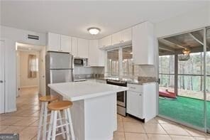 kitchen with a kitchen breakfast bar, light tile patterned floors, white cabinetry, a kitchen island, and appliances with stainless steel finishes