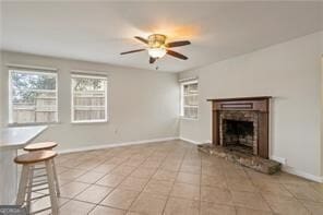 unfurnished living room featuring light tile patterned floors, ceiling fan, a brick fireplace, and baseboards