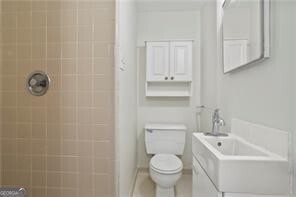 bathroom with toilet, tiled shower, and vanity