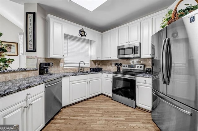3139 Players Dr, Jonesboro, GA 30236 - kitchen with stainless steel appliances, white cabinetry, light wood finished floors, and dark stone counters
