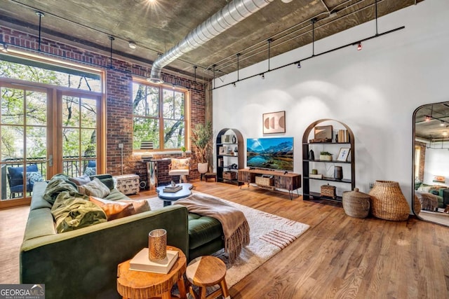 living area with track lighting, brick wall, a high ceiling, and wood finished floors
