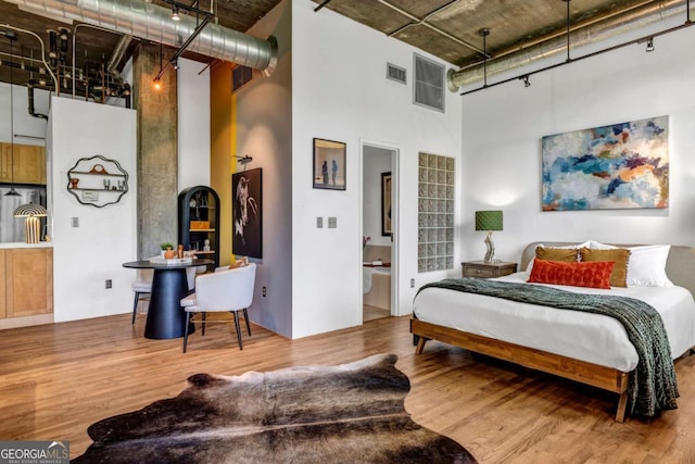 bedroom with visible vents, track lighting, a high ceiling, and wood finished floors