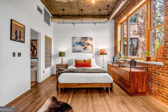 bedroom with brick wall, wood finished floors, a high ceiling, and visible vents