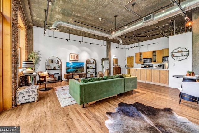 living area featuring visible vents, light wood-type flooring, and a high ceiling