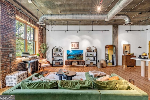 living area with brick wall, a high ceiling, and wood finished floors