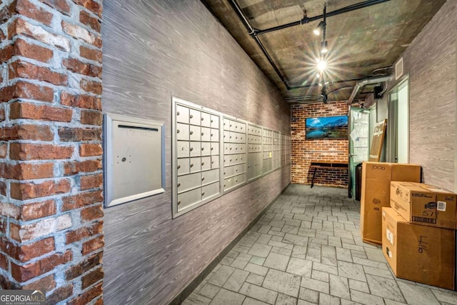 hallway featuring visible vents, mail area, brick wall, brick floor, and rail lighting