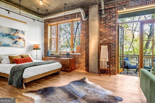 bedroom with brick wall, a towering ceiling, access to exterior, and wood finished floors