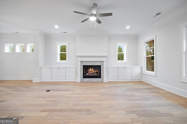 unfurnished living room with light wood-style flooring, crown molding, a glass covered fireplace, and visible vents