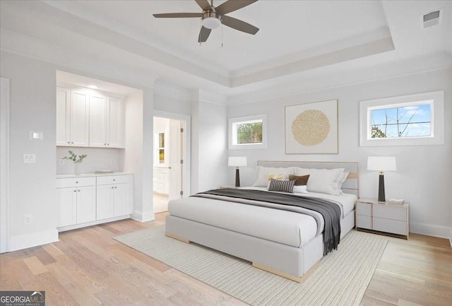 bedroom with a tray ceiling, light wood-style floors, baseboards, and visible vents