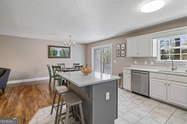kitchen with a notable chandelier, a textured ceiling, a kitchen bar, stainless steel dishwasher, and a sink