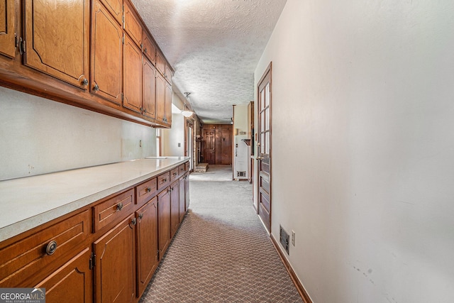 hallway featuring a textured ceiling, carpet flooring, baseboards, and visible vents