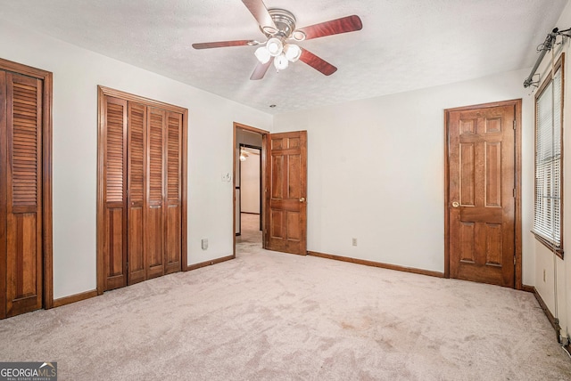 unfurnished bedroom featuring baseboards, multiple closets, carpet flooring, and a ceiling fan