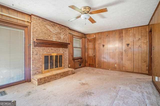 unfurnished living room with a textured ceiling, ceiling fan, carpet floors, wood walls, and visible vents