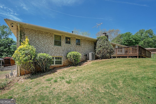 back of house with central AC unit, fence, brick siding, a wooden deck, and a yard
