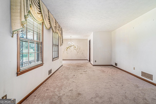 carpeted empty room with a textured ceiling, visible vents, baseboards, and a notable chandelier