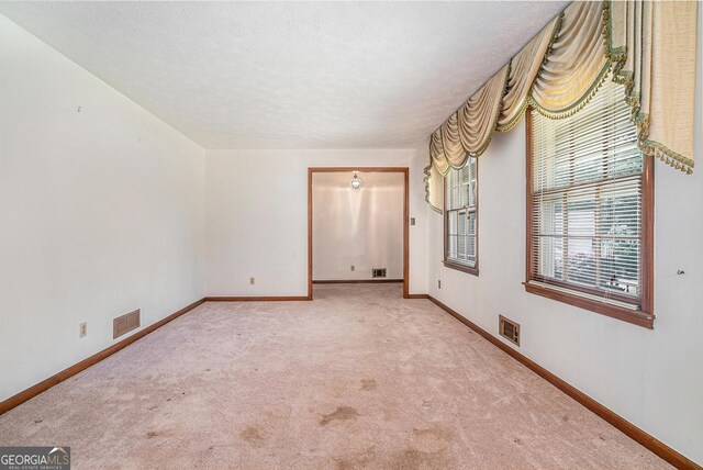 carpeted spare room with a textured ceiling, visible vents, and baseboards