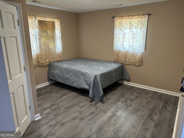 bedroom featuring crown molding, visible vents, baseboards, and wood finished floors