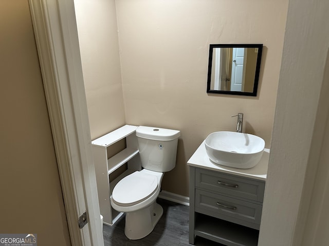 half bath featuring toilet, vanity, wood finished floors, and baseboards