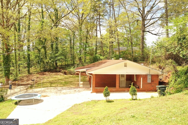 exterior space featuring a trampoline, brick siding, a view of trees, and a front lawn