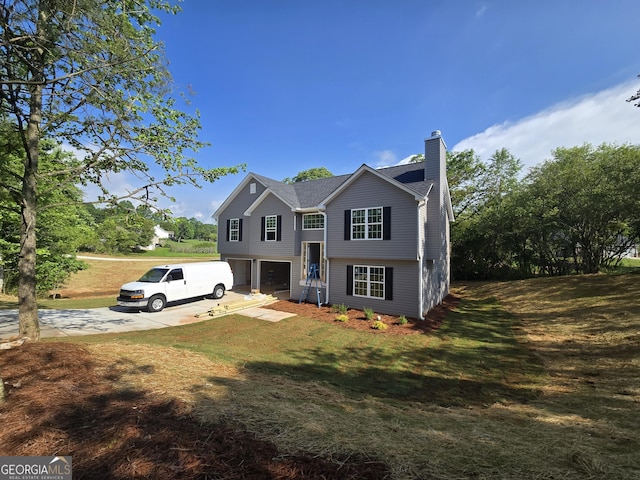 split foyer home featuring concrete driveway, an attached garage, a chimney, and a front lawn