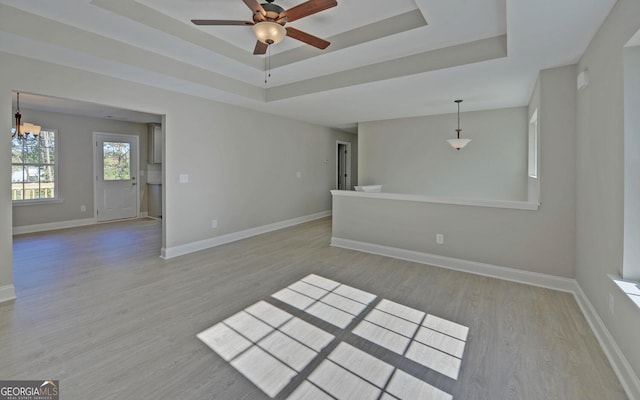 unfurnished living room featuring baseboards, a tray ceiling, wood finished floors, and ceiling fan with notable chandelier