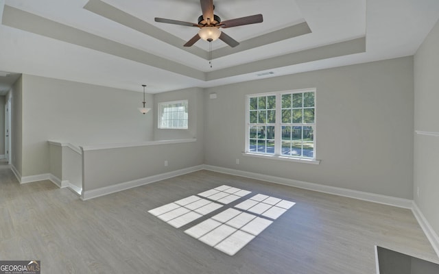 unfurnished room featuring ceiling fan, visible vents, wood finished floors, baseboards, and a tray ceiling