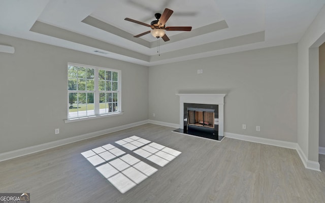 unfurnished living room with ceiling fan, visible vents, a fireplace, wood finished floors, and a tray ceiling