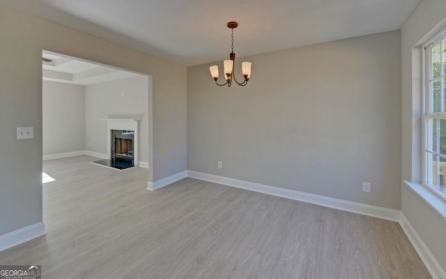 empty room featuring light wood-style floors, a fireplace with flush hearth, baseboards, and a notable chandelier