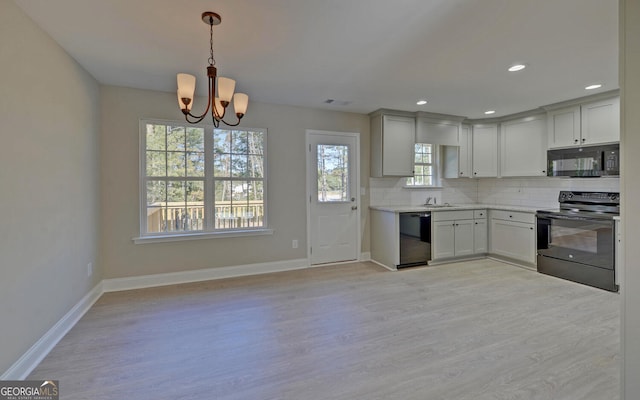 kitchen with a wealth of natural light, black appliances, light wood-style flooring, and a notable chandelier