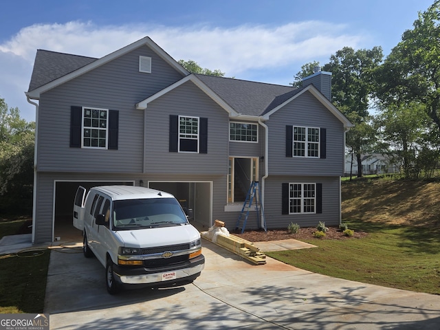 raised ranch featuring a garage, a shingled roof, a chimney, and driveway