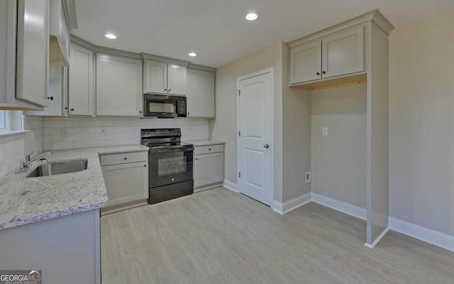kitchen with a sink, baseboards, black appliances, and light stone counters