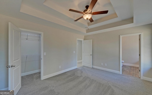 unfurnished bedroom with carpet flooring, a raised ceiling, baseboards, a spacious closet, and a closet