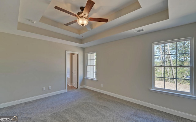 empty room featuring visible vents, a raised ceiling, plenty of natural light, and ceiling fan