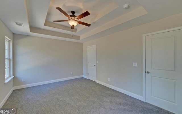 empty room featuring carpet floors, a ceiling fan, a tray ceiling, and a healthy amount of sunlight