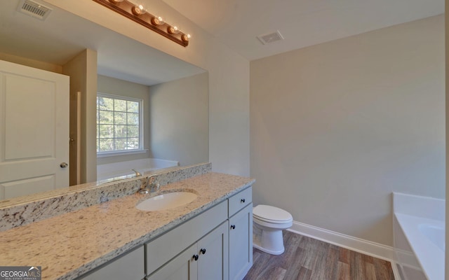 bathroom featuring visible vents, wood finished floors, toilet, baseboards, and a tub